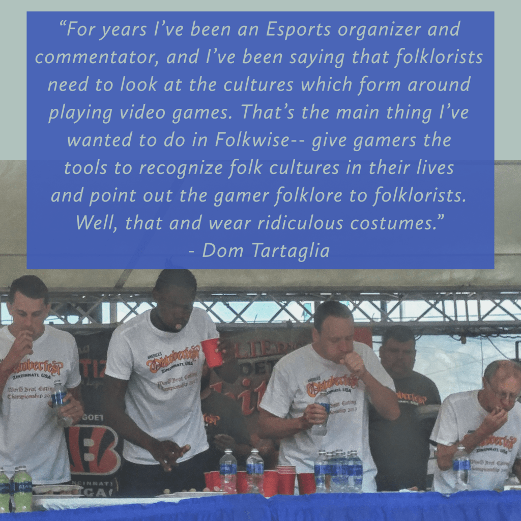 Image of several people in a line at a hotdog eating contest actively eating hotdogs behind a table. White text on the image with blue background reads “For years I've been an esports organizer and commentator, and I've been saying that folklorists need to look at the cultures which form around playing video games. That's the main thing I've wanted to do in Folkwise-- give gamers the tools to recognize folk cultures in their lives and point out the gamer folklore to folklorists. Well, that and wear ridiculous costumes. - Dr. Dom Tartaglia”