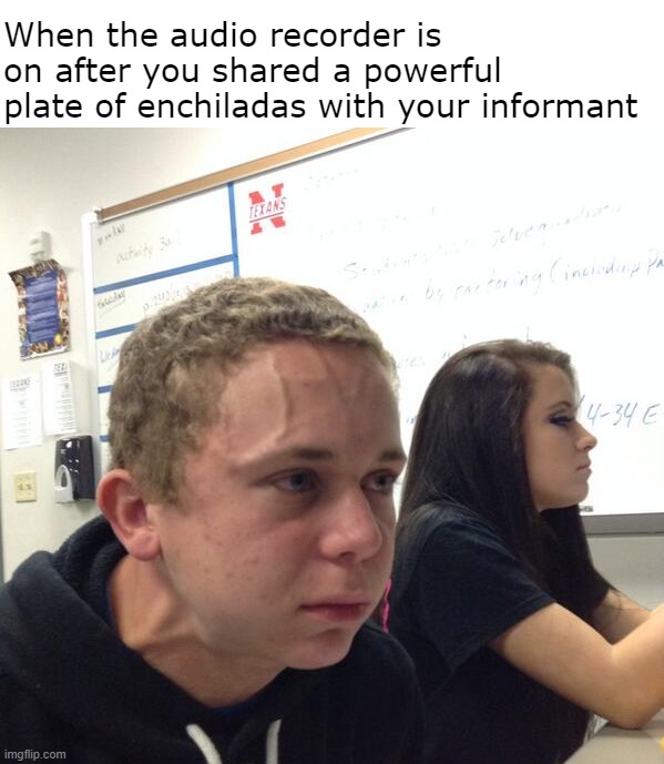 an image of a male student sitting in a classroom with an extremely red, strained facial expression, with visible veins. He is wearing a black jacket, and there is a female student with a neutral facial expression and a whiteboard in the background. Text reads: when the audio recorder is on after you shared a powerful plate of enchiladas with your informant.